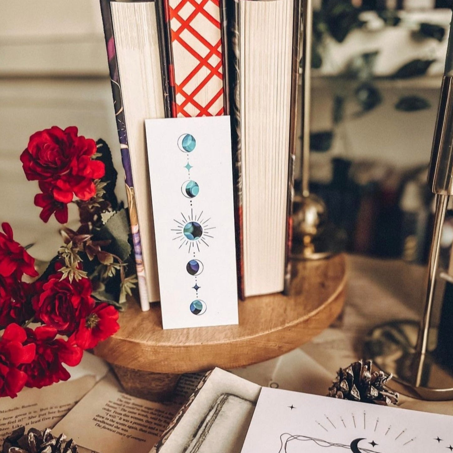 A white bookmark with a blue lunar phase on. Books in the background