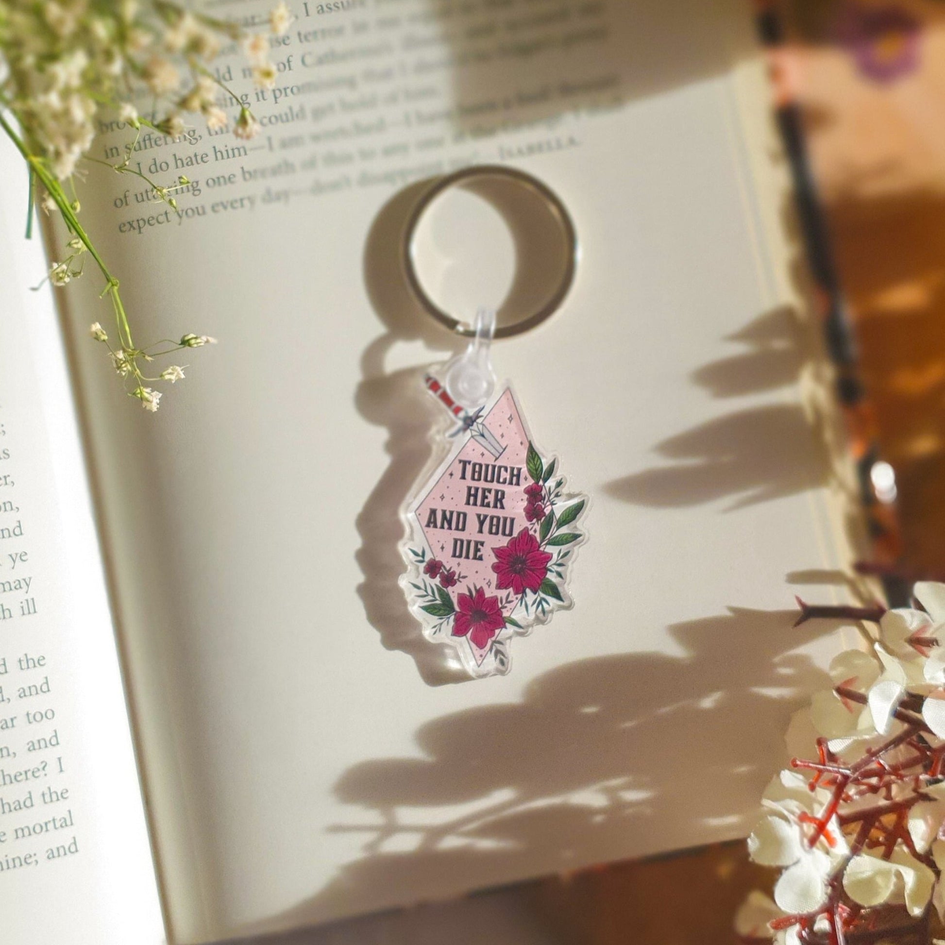 Bookish acrylic keyring with "Touch her and you die" quote and flowers. Pink colour and silver keychain.