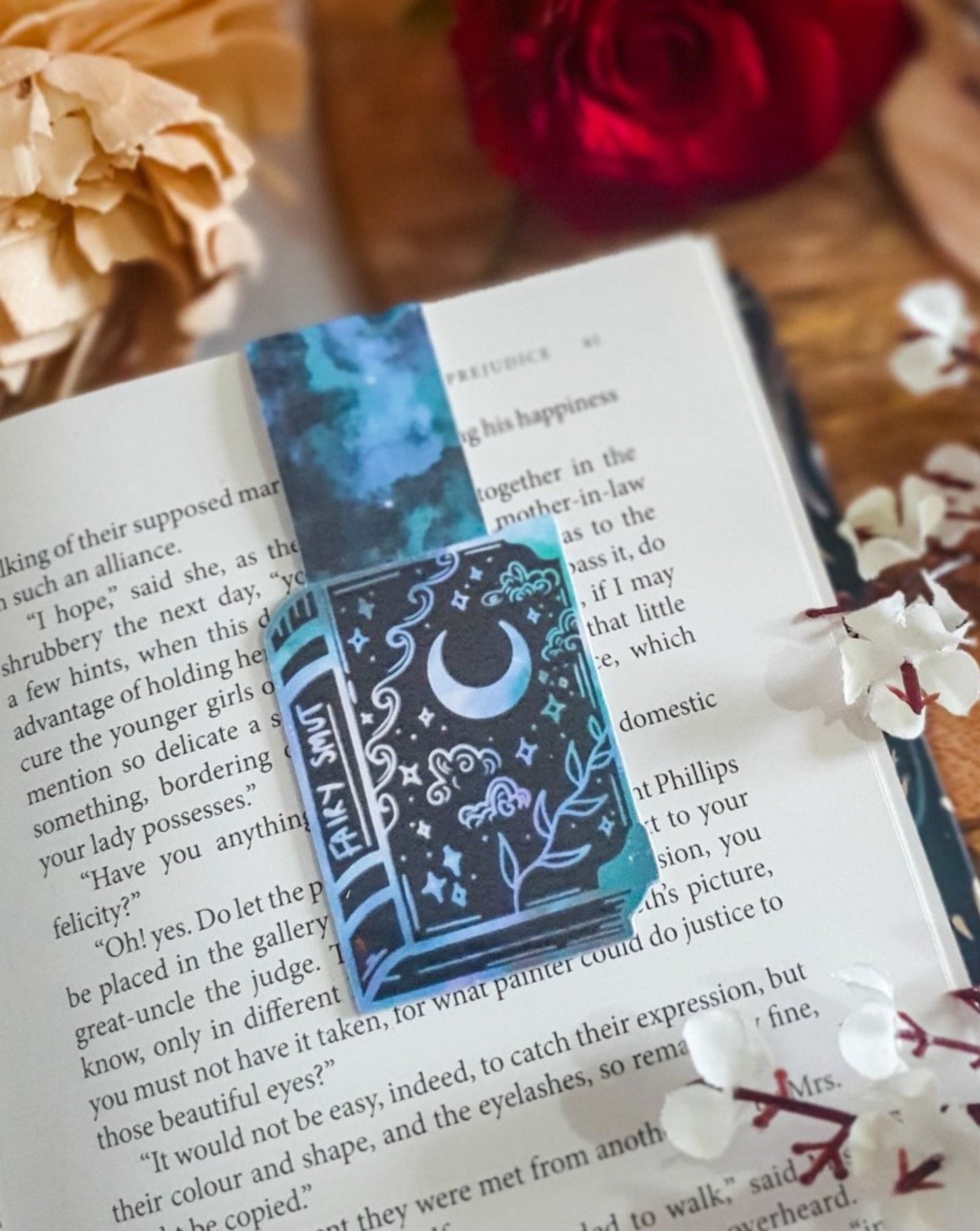 magnetic bookmark in the shape of a book with white and green clouds, stars, vines and moons on the book. The spine says fairy smut.