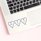 a white sticker with three black heart outlines. Inside the hearts it says Rhys, Az, Cas. The sticker is on a laptop.