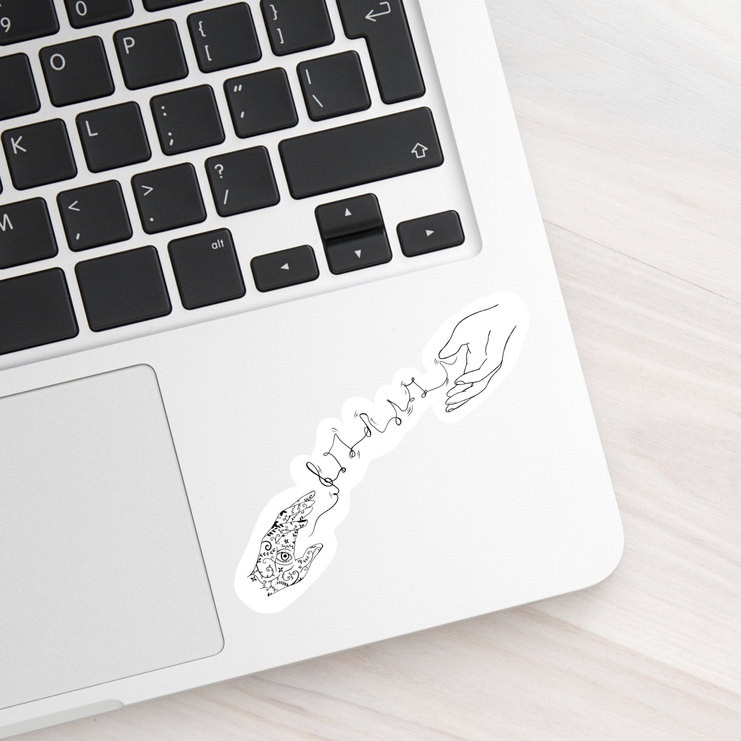 A laptop with a black and white sticker on. An outline of two hands connected by a wave of musical notes. One hand has tattoos on it. The sticker is on a laptop